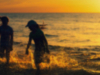 A gauzy photograph of two children playing in the surf. The sun is setting and they are mostly swallowed in shadow
