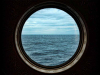 A photograph of a porthole window on a ship, looking out at the ocean