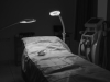 A photograph of a hospital bed bathed in light in a room swathed in shadow