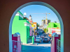 A photograph looking down a colorful city street through a painted archway