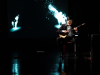 A man seated on a mostly darkened stage playing a saz