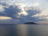 An island, shrouded in darkness, a light can be seen on the sea surrounding peeking in from the edges