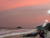 A photograph of a beach at sunset with a lighted highway running past it