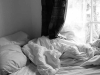 An unamde bed, bathed in light from a nearby window