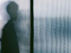 A human figure in silhouette through opaque textured glass