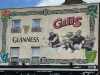 A mural on the side of a building. The mural shows sports figures and the text reads: Guiness. Gills.