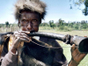 A photograph of an indigenous man blowing into a crude horn