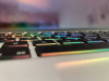 A close-up detail of a computer keyboard that is underlit by rainbow colored LEDs