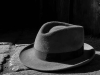 A man's hate sits partially illuminated by sunlight on a table.