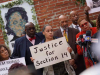 A photograph of a number of African Americans at a press conference. The woman in the center holds a sign that reads, "Justice for Section 14"