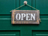 A weather wooden sign that reads, "Open" hanging on a door painted forest green