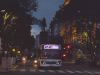 A photograph of a bus traversing a crowded city street at dusk