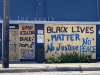 Spray painted words adorn the side of a boarded up building. Text reads: Stop killing black people. Black Lives Matter. No justice. No peace.