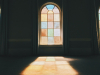 A photograph of a stained glass window from inside a darkened room with the color and light through the window projecting on to the floor