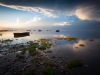 A boat floats in a desultory natural port as the sun begins to crest above the horizon