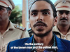 A still from a movie. A dark-skinned man, dressed in a blue shirt, is flanked on either side by men dressed in military garb. The text (which is a subtitle) reads, "It is the century of the brown man and the yellow man."