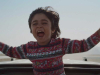 A still image of a boy with his arms outstretched coming out of the top of a moving car