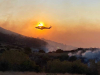 A helicopter hovers above a smoldering, mountainous landscape. The sun is positioned just such that the helicopter appears to be on fire.