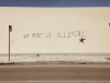 A photograph of a wall with the words, "No one is illegal" spray painted on it