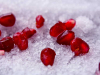 A photograph of dark crimson pomegranate seeds delicately laid out on snow