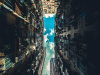 A photo looking upward between two very tall buildings with a blue sky, dotted with clouds, emerging in the thin line between them