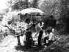 A black and white photograph of men working to secure an umbrella on a film set located in a jungle