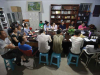 A group of people sit around a table, many of them looking toward the head of the table