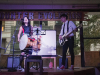 Two musicians, a woman playing a bass drum and a man playing a bass guitar, perform on stage