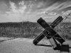 A black and white photo of a cross-shaped road obstacle, wrapped in barbed wire