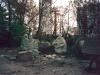 A collection of statues of resting soldiers, tucked into a small grove of trees with trash and industrial detritus strewn about