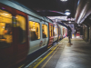 A lone figure stands in the polarized light of the subway at night as a train passes in front of him