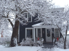 A blue house with snow on the roof and trees.