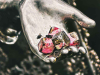 A photograph of a cluster of metal nuts, covered in some kind of red substance, inside of the hand of a metal statuary. A few flies linger in the palm.