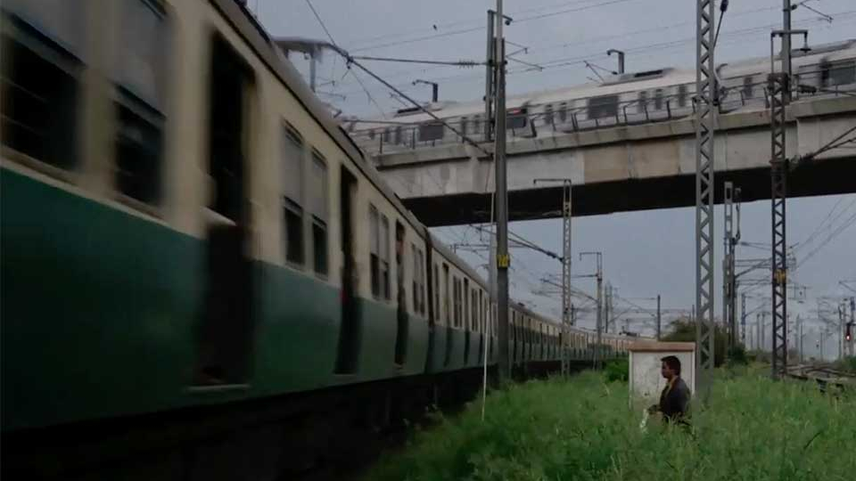 A man wades through a grassy field to approach a train in the city.