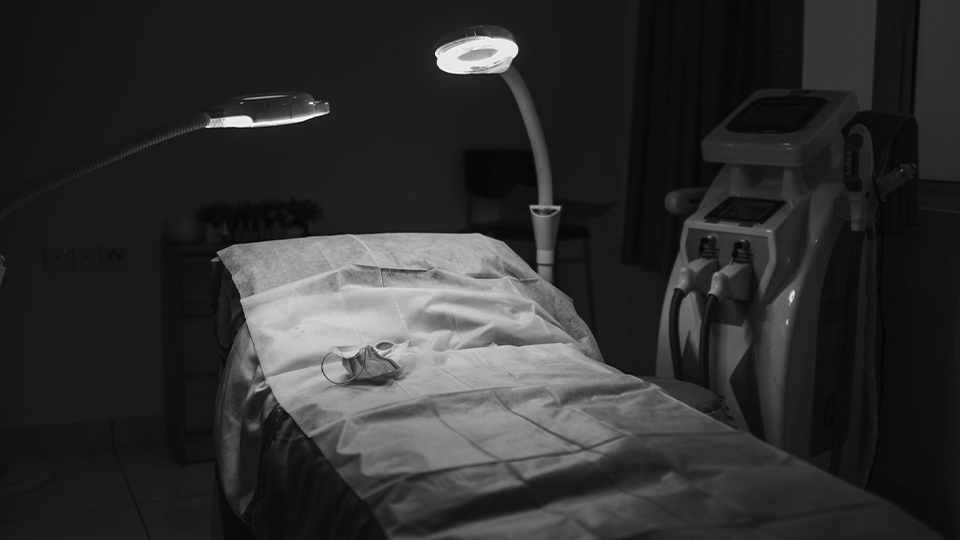 A photograph of a hospital bed bathed in light in a room swathed in shadow