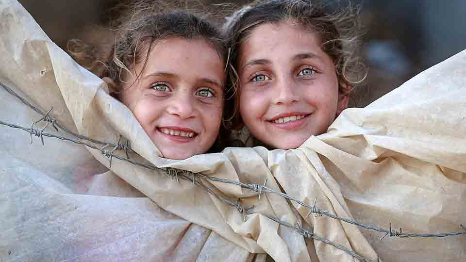 Two children peer out of a canvas tent 