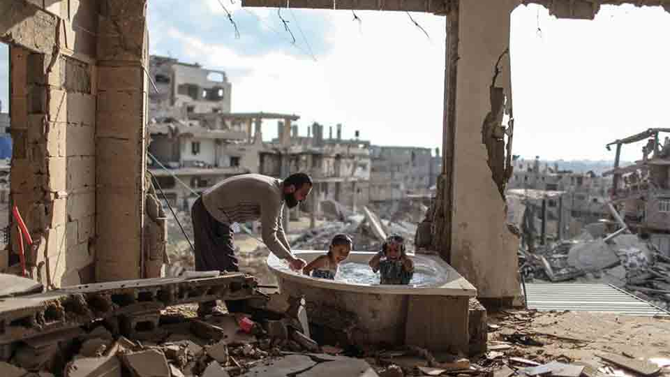 A man bathes two children in the rubble of a bombed-out apartment