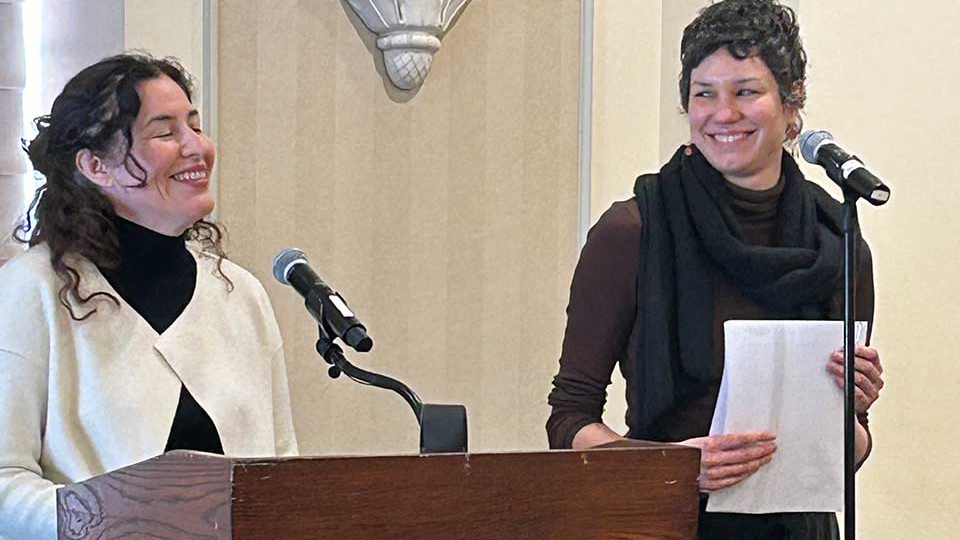 Guadalupe Nettel stands at the lectern laughing while Rosalind Harvey watches her, smiling