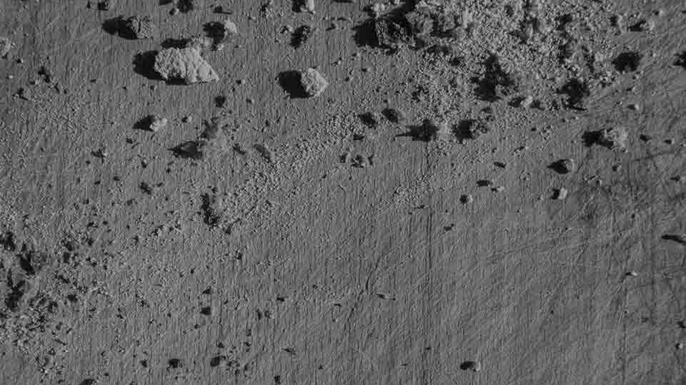 An aerial photo of a gray landscape where rocks cast shadows on the ashen ground below
