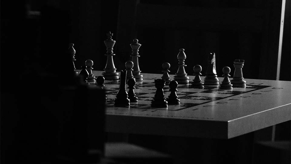 A chessboard in a room consumed by shadows