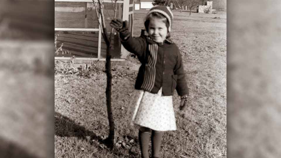 A black and white photograph of a young girl waving at the camera
