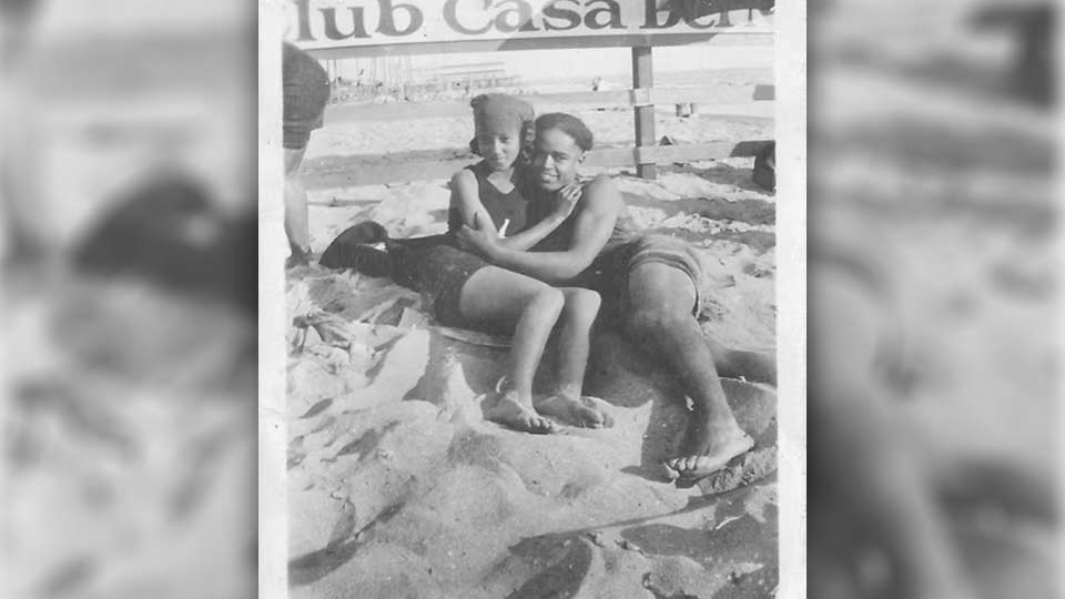 A black and white photo of a man and a woman embracing while they lay in the sand