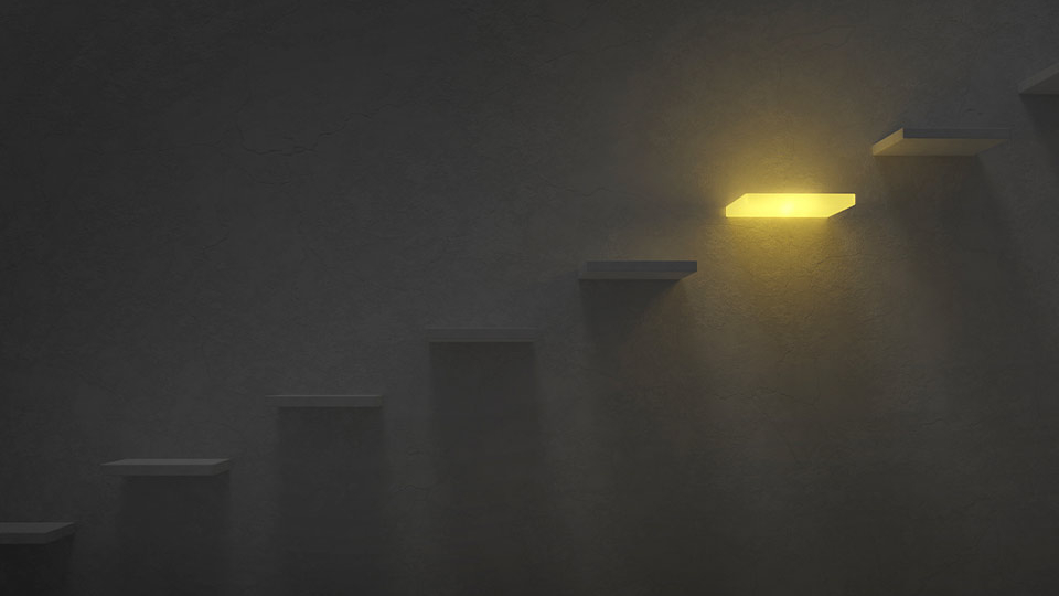 A photograph of an art piece. Stairs embedded into a wall rise in the shadow until the next to last step is lit in the dark