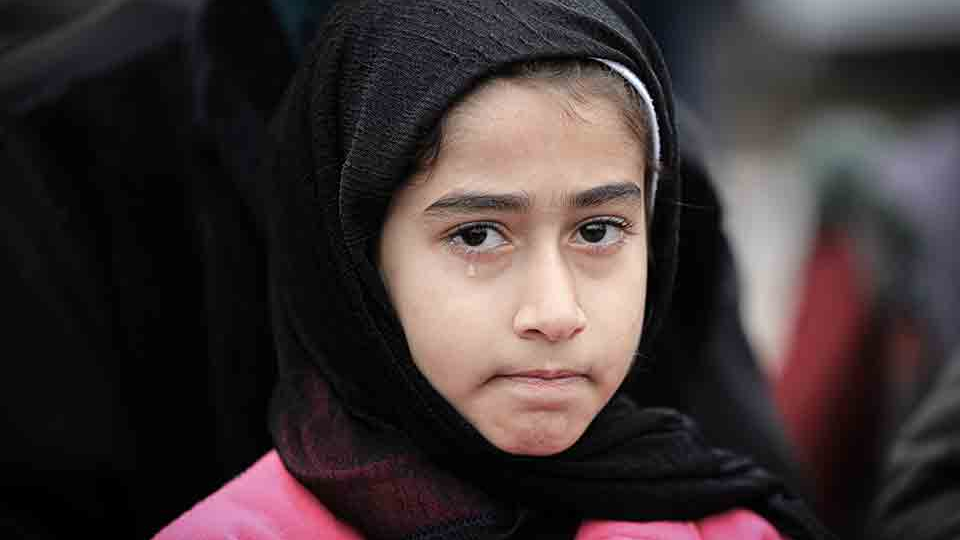 A young girl, veiled in black, looks at the viewer glumly with a single tear running down her face