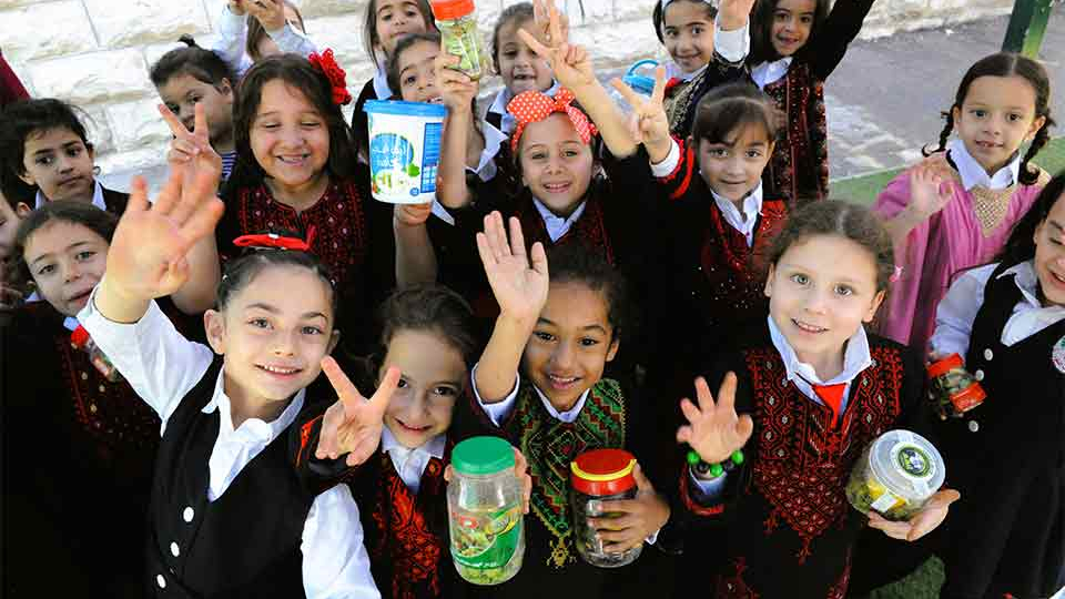 A photograph of a group of Palestinian children in school uniforms smiling for the camera which is above them