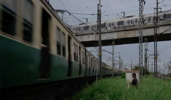 A man wades through a grassy field to approach a train in the city.