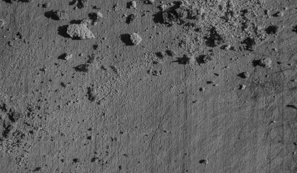 An aerial photo of a gray landscape where rocks cast shadows on the ashen ground below