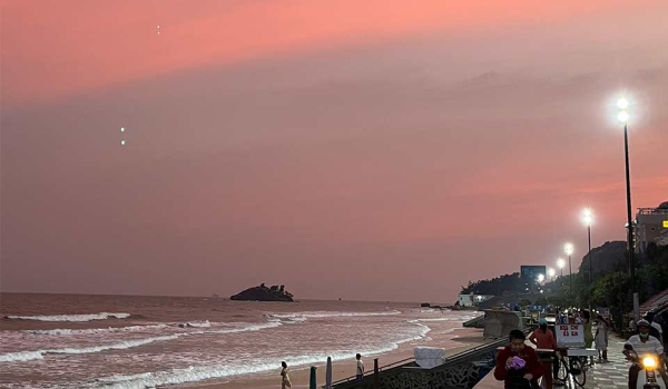 A photograph of a beach at sunset with a lighted highway running past it