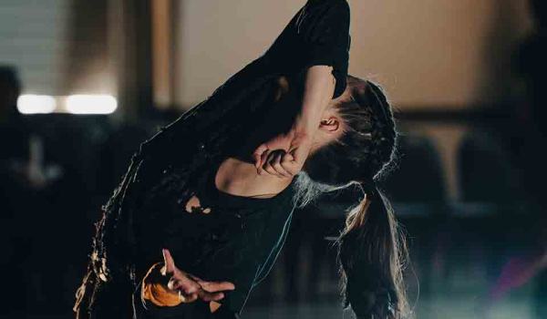 A dancer hides her face behind her elbow as she arcs her back toward the sky