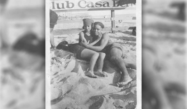 A black and white photo of a man and a woman embracing while they lay in the sand